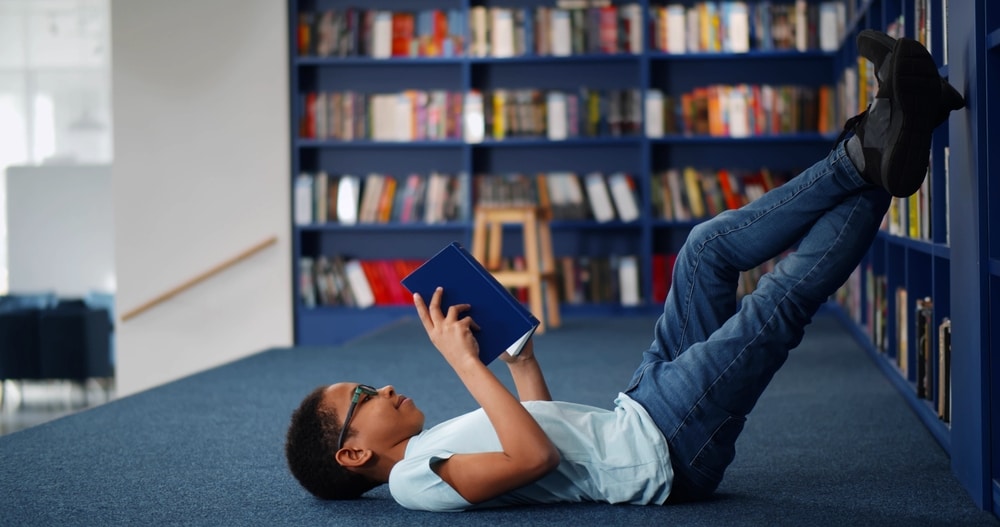 African american,Boy,Lying,On,Floor,And,Reading,Book,In,Modern