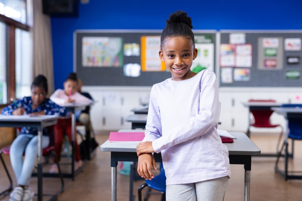 At,School,,Smiling,African,American,Girl,Near,Desk,,Diverse,Classmates