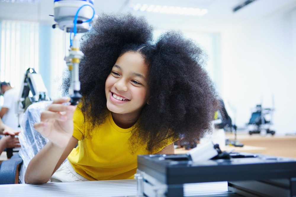 Happy,African,American,Girl,Interacting,With,Robotic,Arm,In,Tech