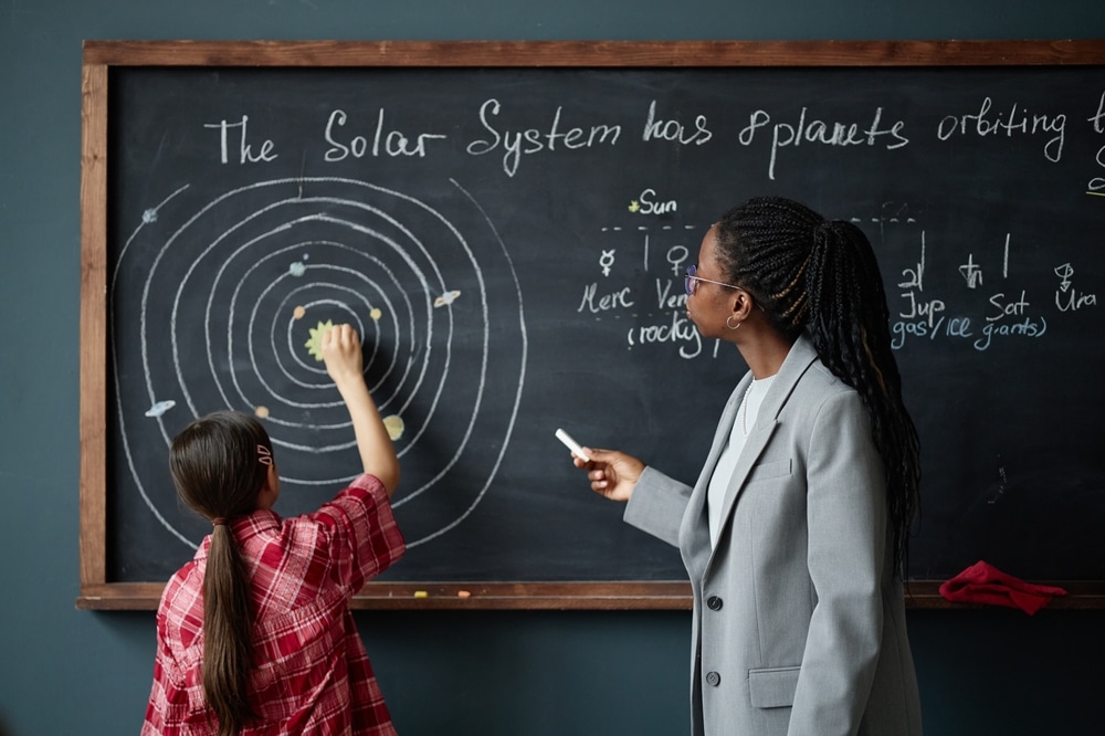Black,Woman,Teacher,Explaining,Solar,System,Diagram,On,Chalkboard,While